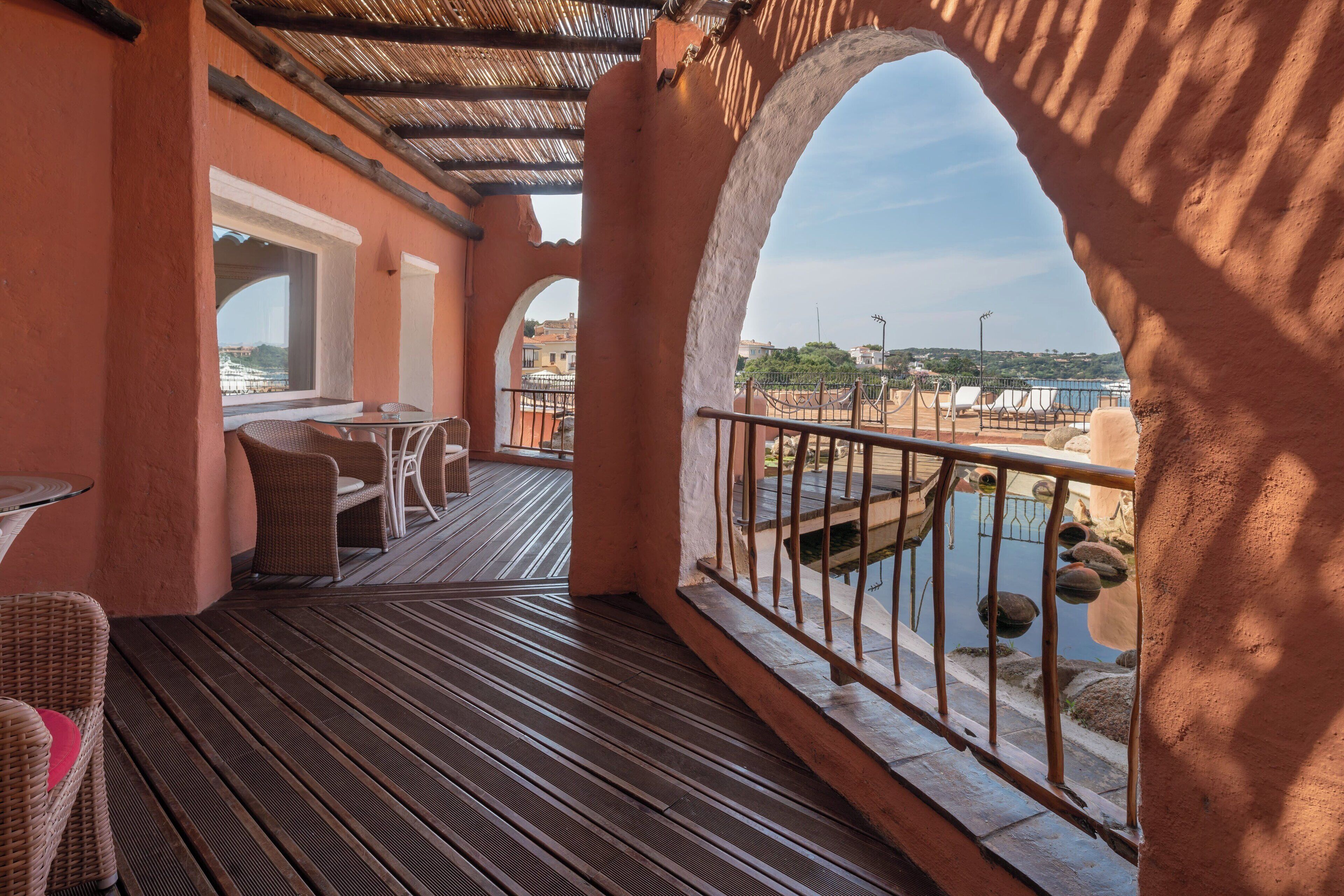 A covered outdoor area with a wooden deck, wicker furniture, and a view of a body of water and distant buildings.