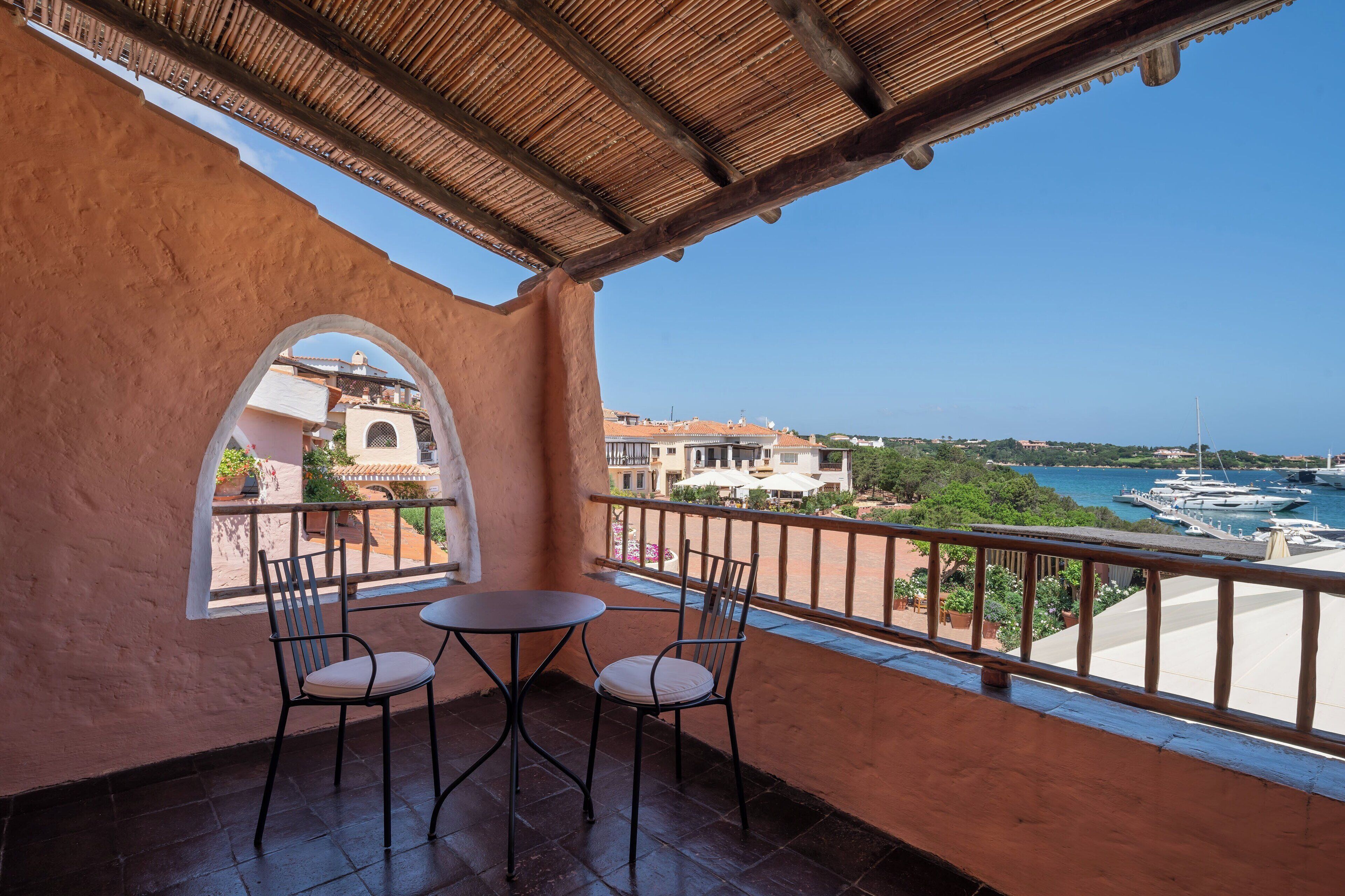 A balcony with two chairs and a table, overlooking a marina with boats and buildings in the background.