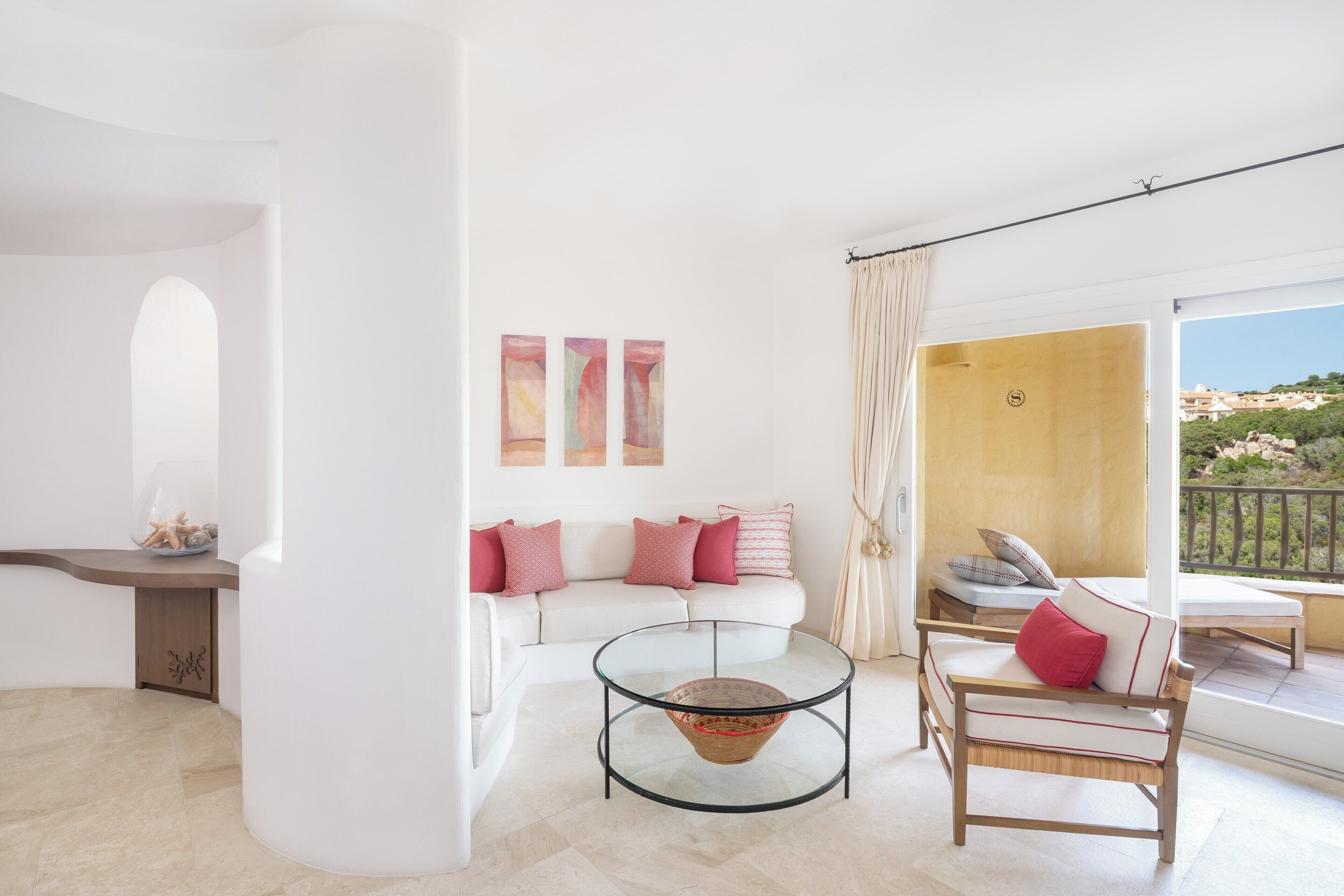 Ein modernes Wohnzimmer mit einem weißen Sofa, einem Glastisch und einem Holzstuhl. Es gibt einen Balkon mit Blick auf die Landschaft.