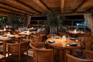 Un restaurante con mesas y sillas de madera, mesas iluminadas con velas y vistas al agua de noche.