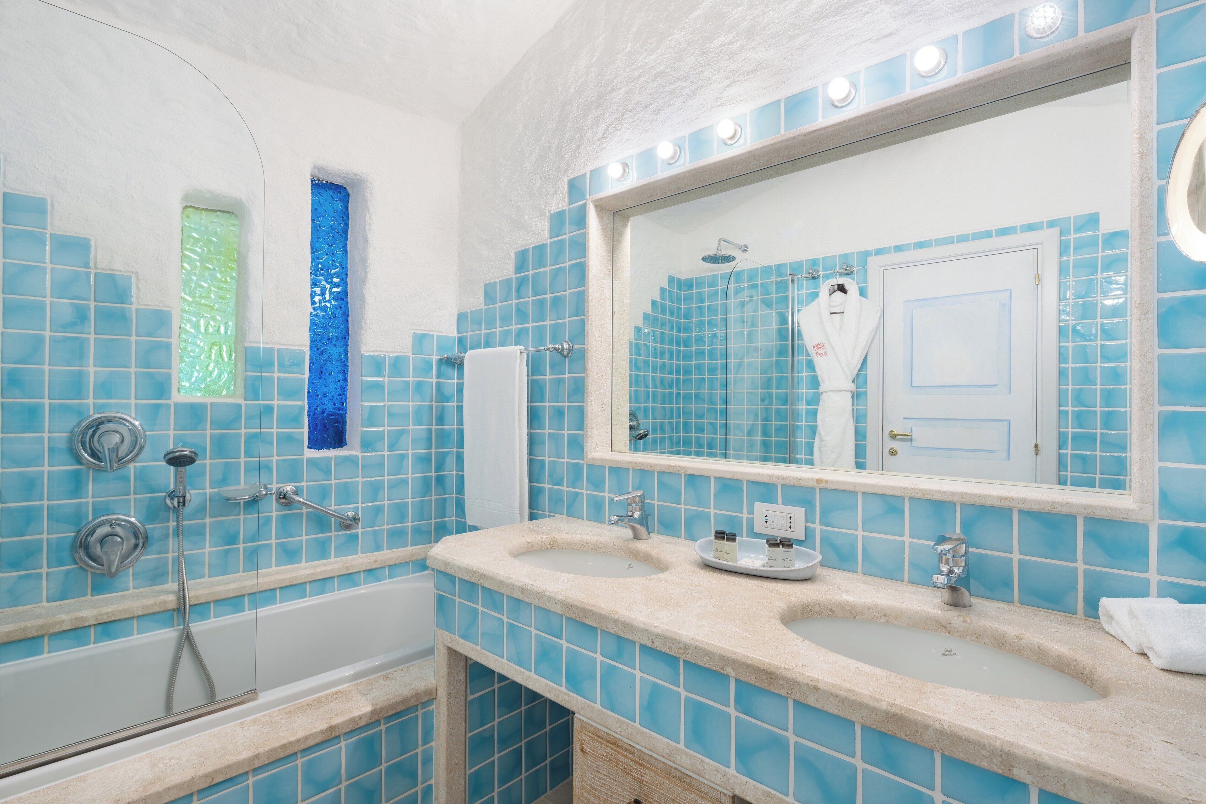 A bathroom with blue tiles, a large mirror, a bathtub, and a sink with a towel hanging on the wall.