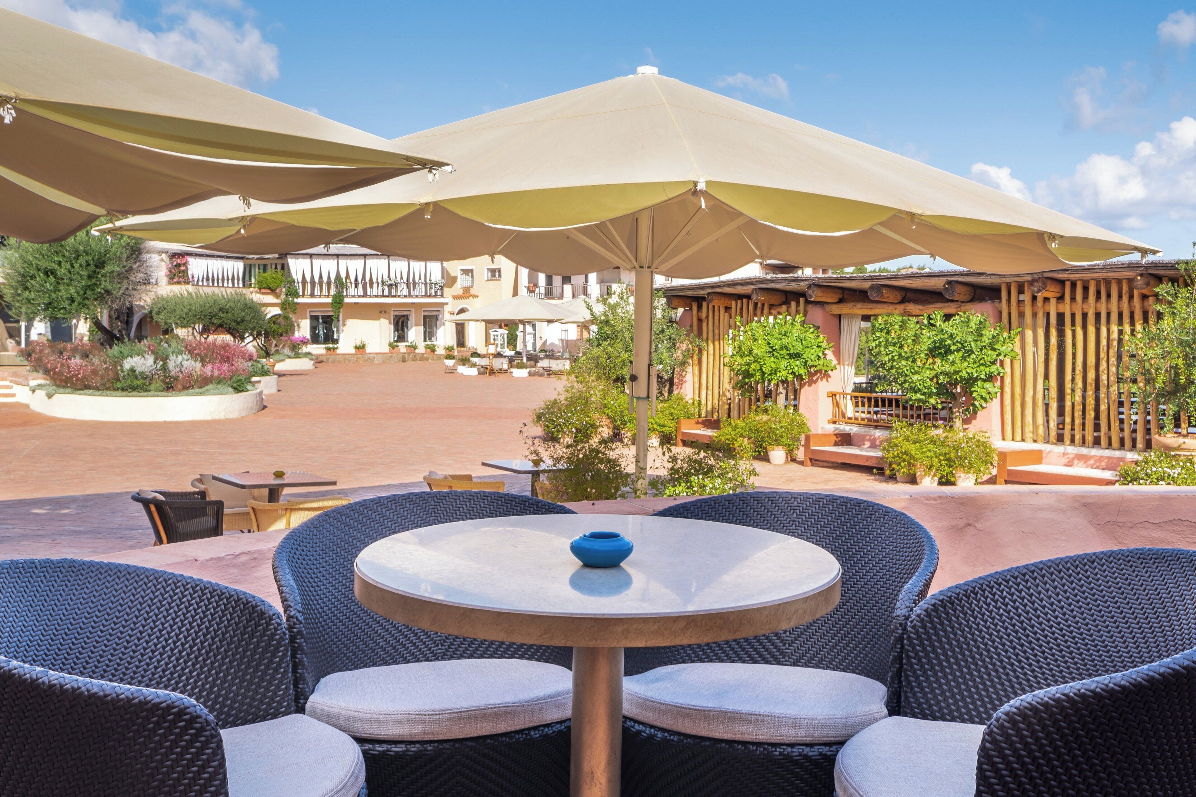 An outdoor patio area with round tables and chairs, large umbrellas, and a building in the background.