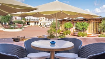 An outdoor patio area with round tables and chairs, large umbrellas, and a building in the background.