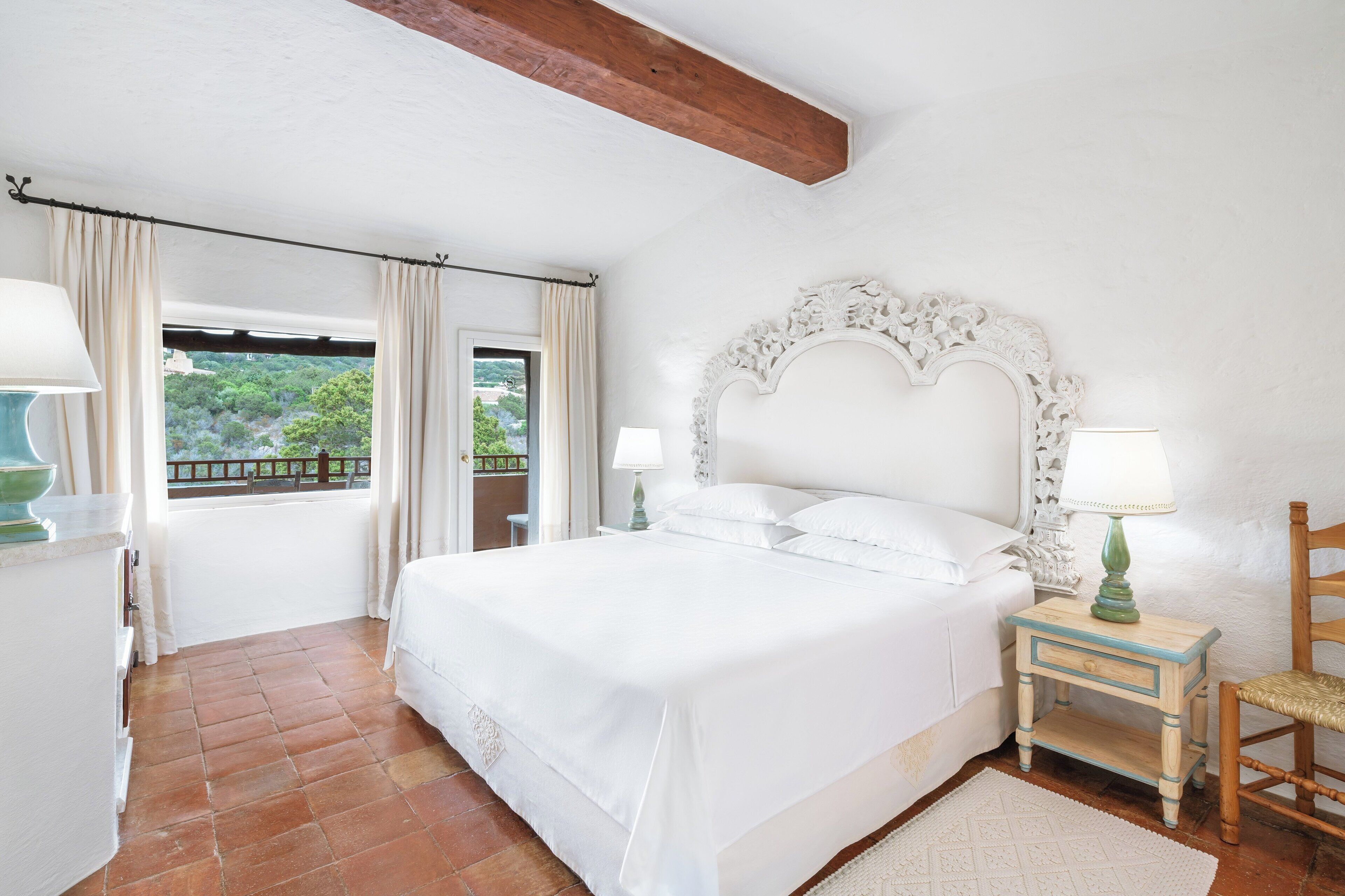 Une chambre à coucher avec un grand lit, deux tables de chevet avec des lampes, une chaise en bois et une vue sur la verdure par la fenêtre.