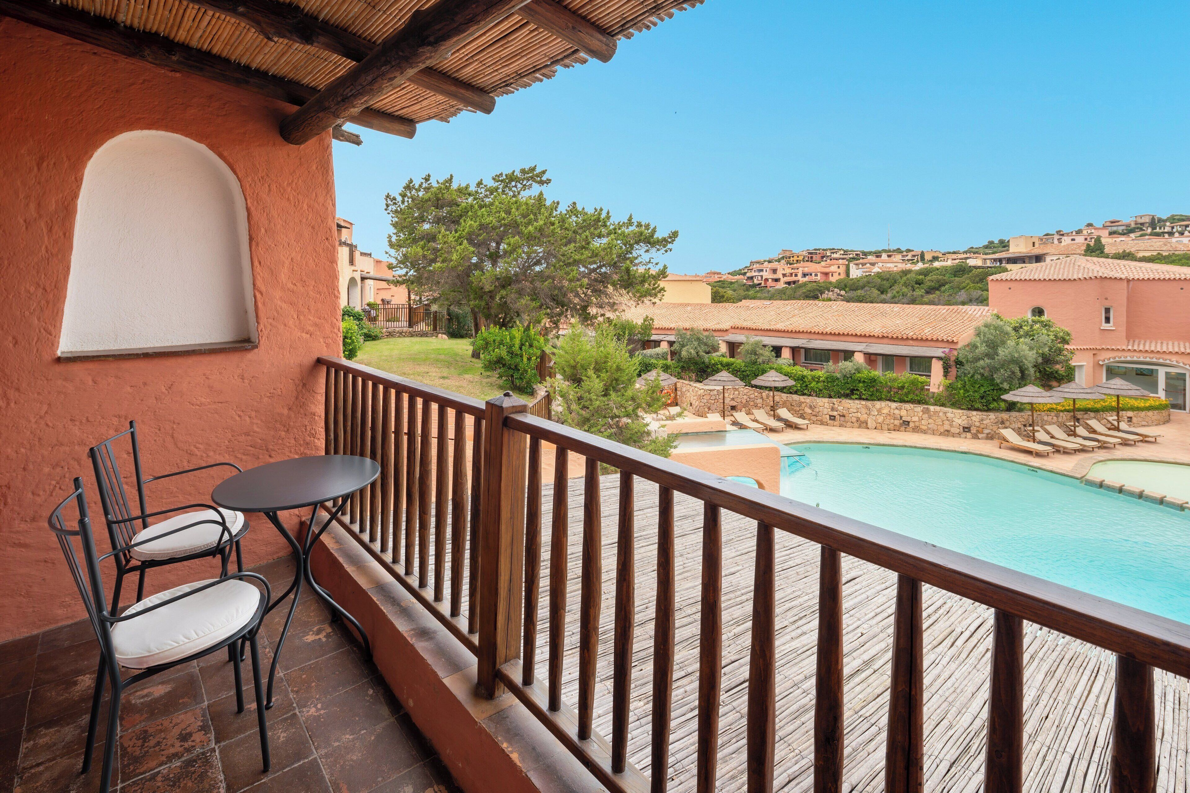 Ein Balkon mit Holzwertlauf, Blick auf einen Pool und eine Hügellandschaft mit Gebäuden.