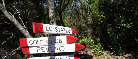 Señal direccional con tres flechas indicando diferentes destinos: Lu Stazzu, Golf Club Pevero y Romazzino.