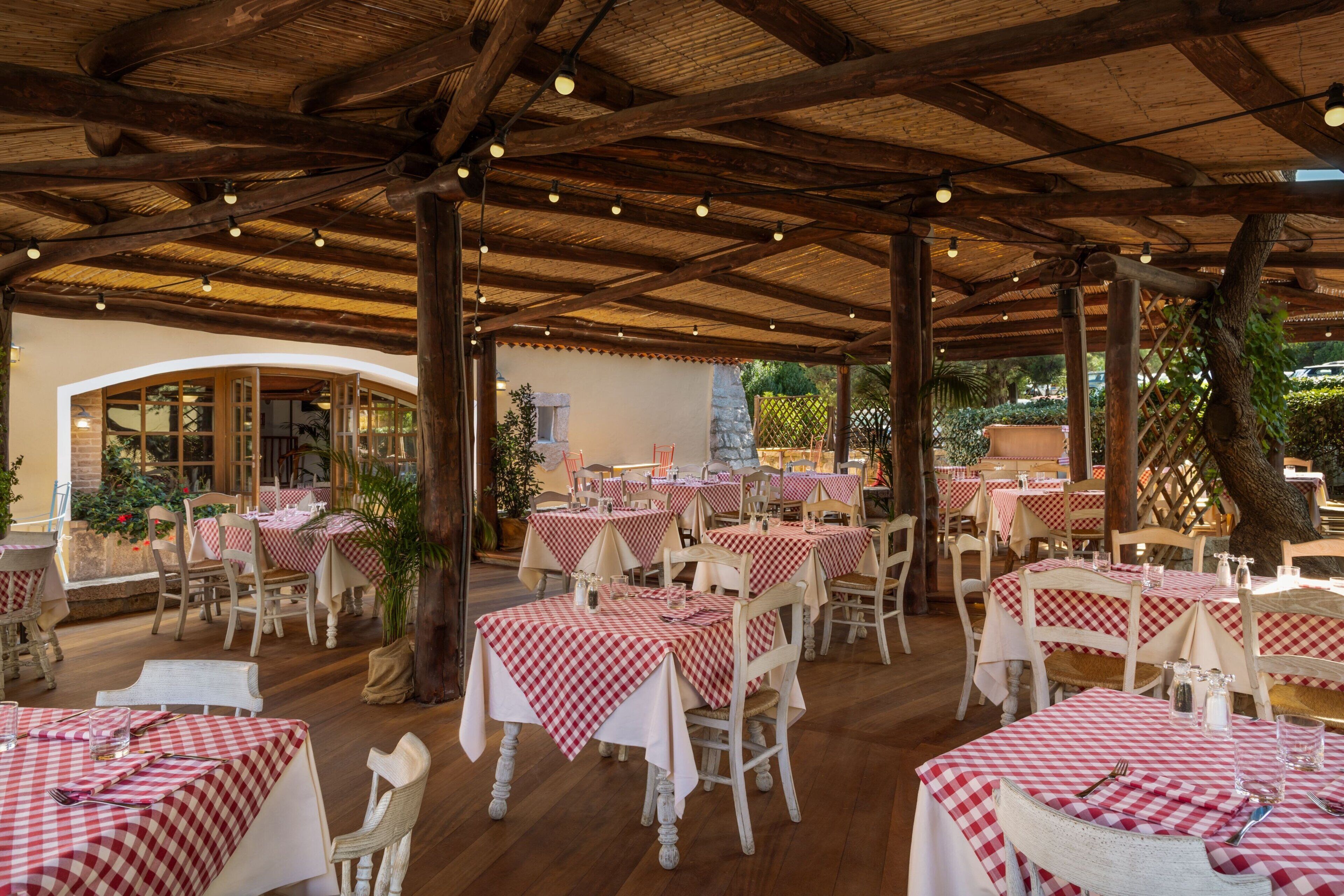 Um restaurante ao ar livre com toalhas de mesa xadrez, cadeiras de madeira e um teto de madeira rústica.