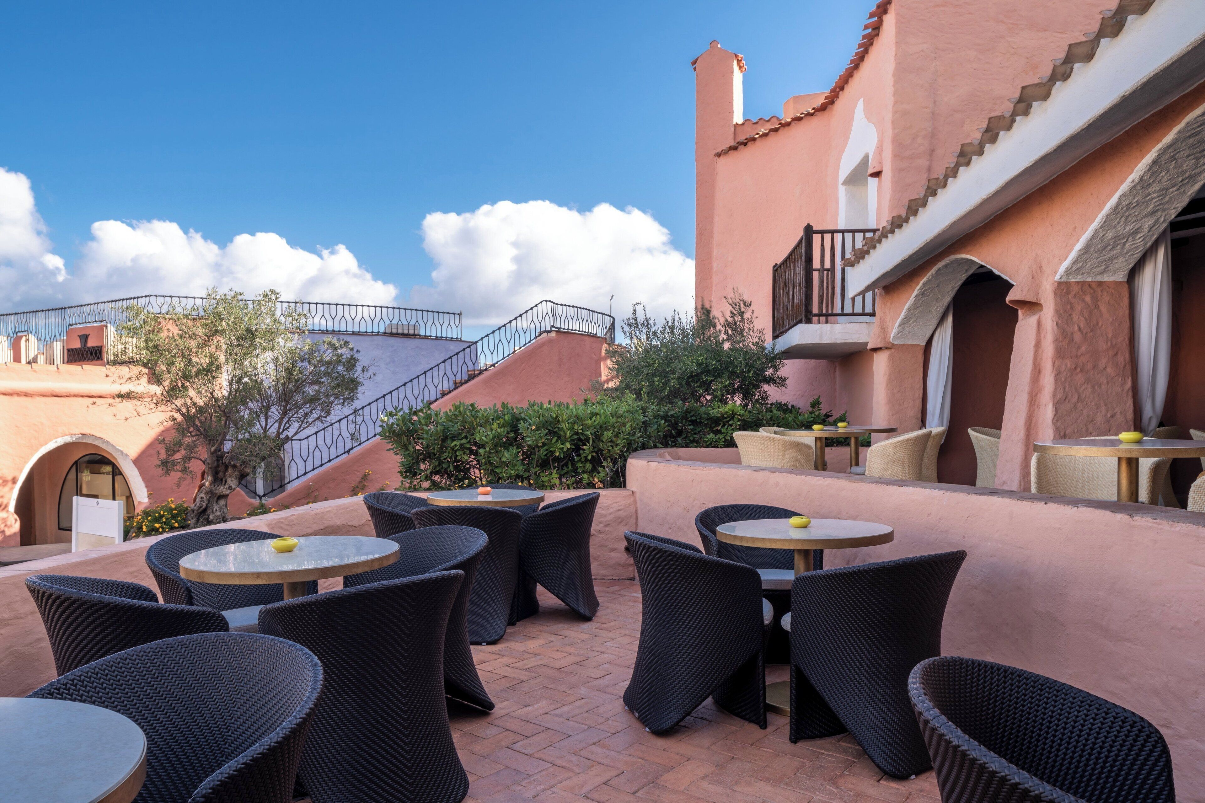 An outdoor patio with wicker furniture and a view of a pink building with a balcony.