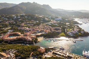 An aerial view of a coastal town with a marina, buildings, and mountains in the background. - Cervo Hotel, Costa Smeralda Resort (Arzachena)