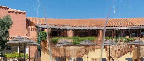 A pool with water jets, lounge chairs, and a building with a tiled roof.