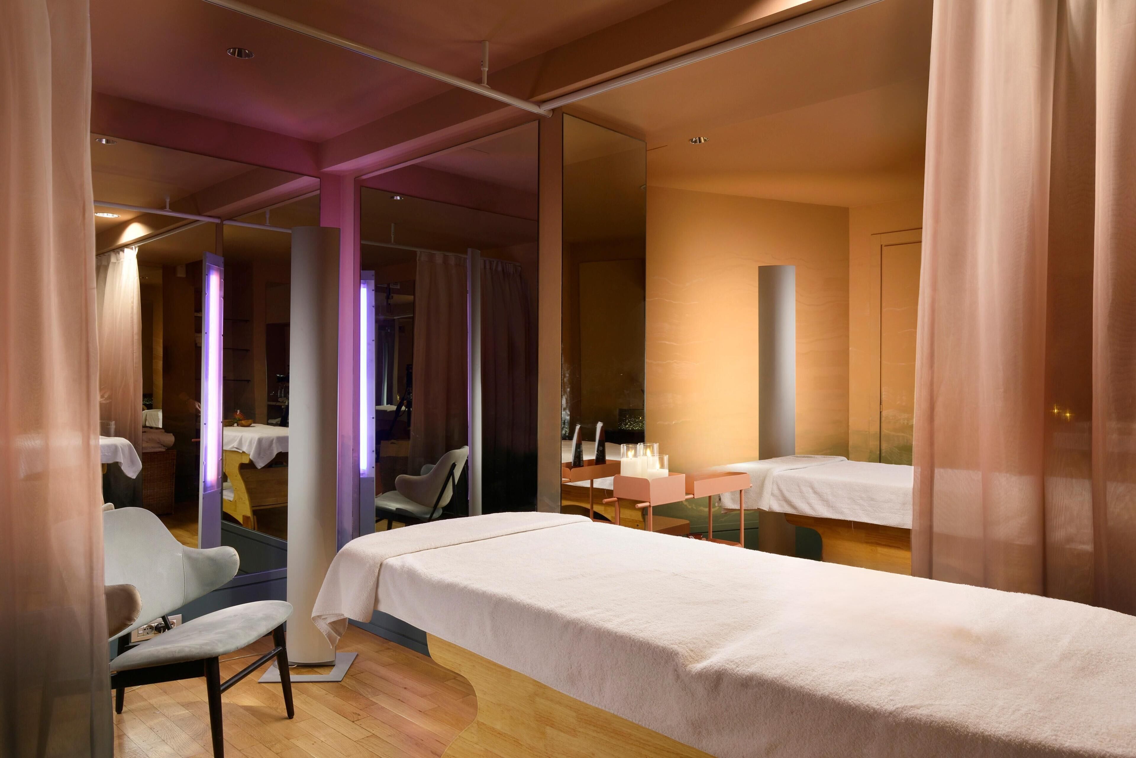 Een moderne hotelkamer met een bed, een stoel, een bureau en een grote spiegel.