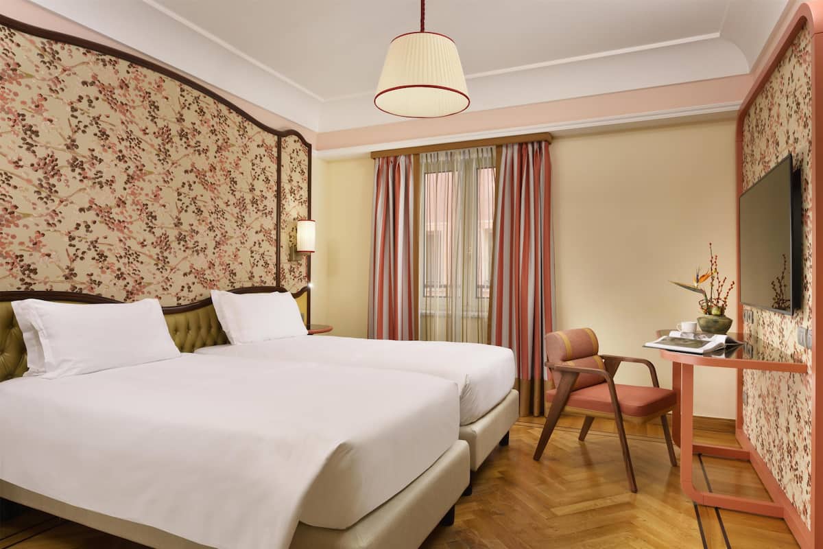 Una habitación de hotel con una cama grande, un escritorio con silla, un televisor y una ventana con cortinas.