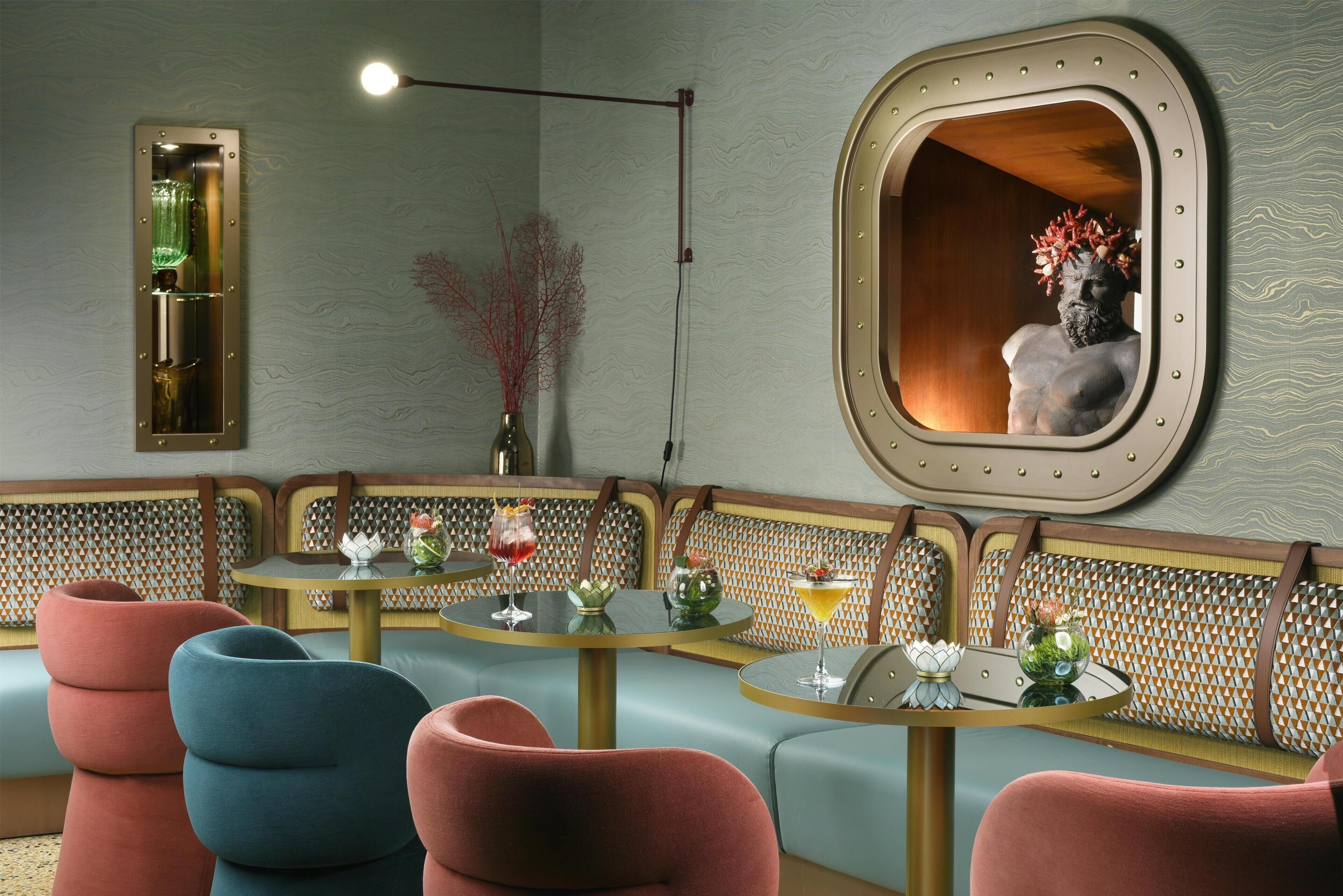 A room with a seating area featuring cushioned benches and round tables, a wall-mounted mirror, and a light fixture.
