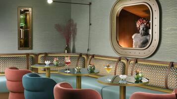 A room with a seating area featuring cushioned benches and round tables, a wall-mounted mirror, and a light fixture.