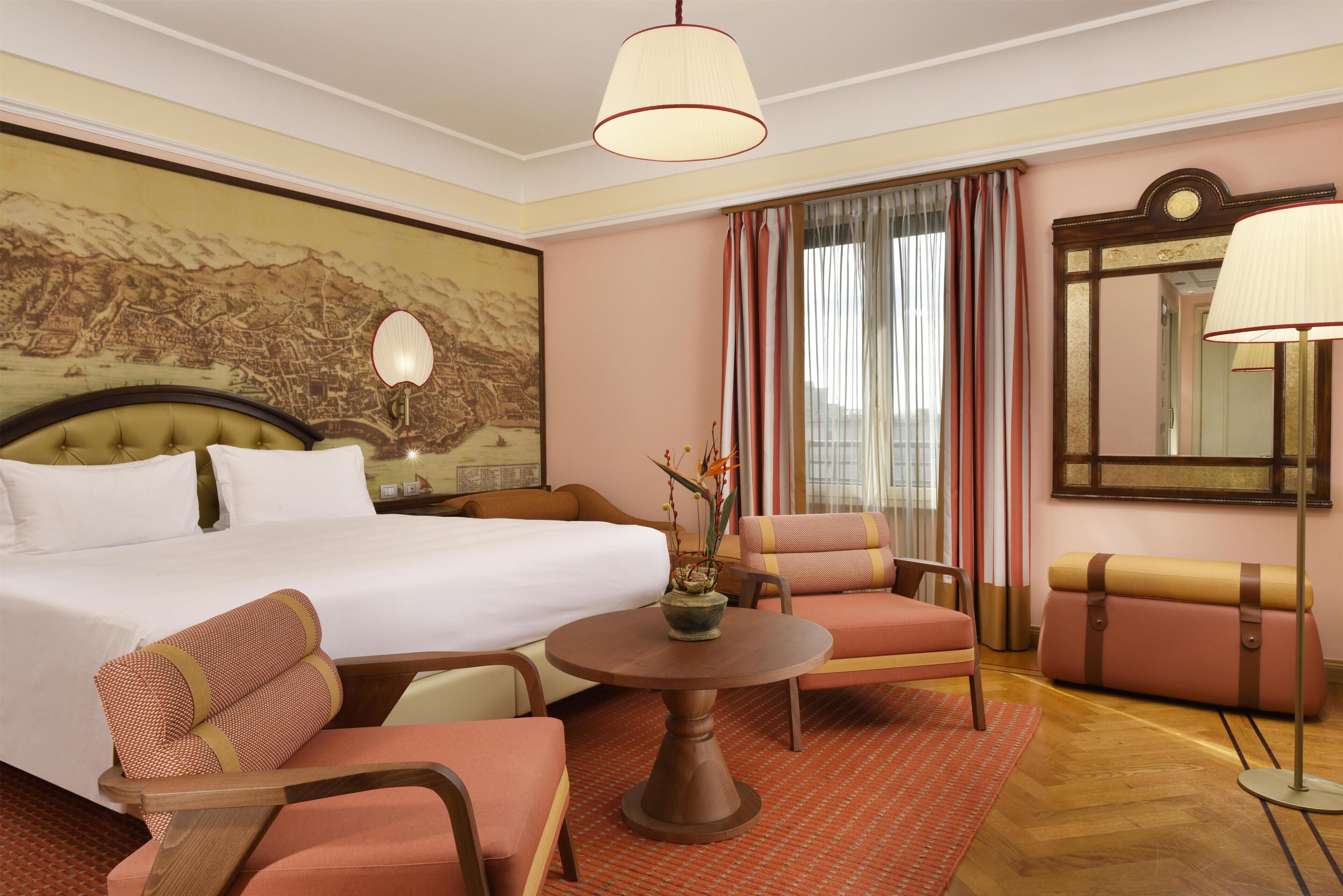 Quarto de hotel com uma cama, uma mesa redonda, duas cadeiras, um sofá, um espelho e um mapa na parede.