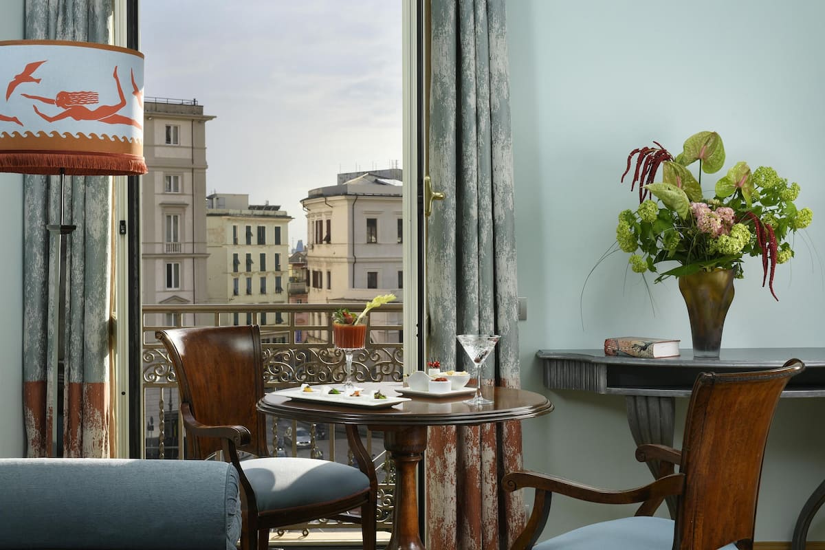 Un balcón con una mesa lista para comer, un florero con flores y vistas a edificios.