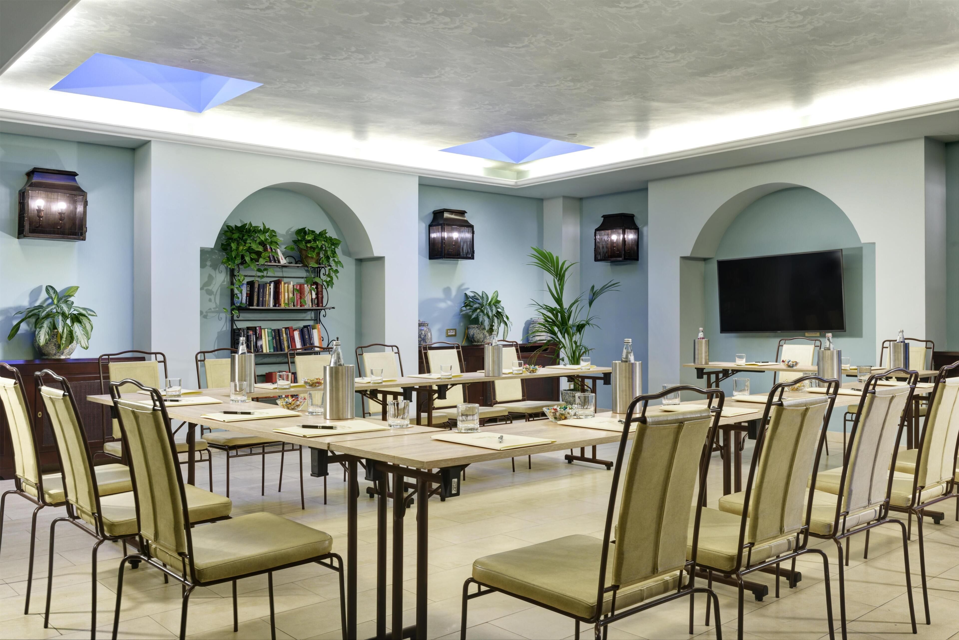 A conference room with tables and chairs, a bookshelf, potted plants, and a television.