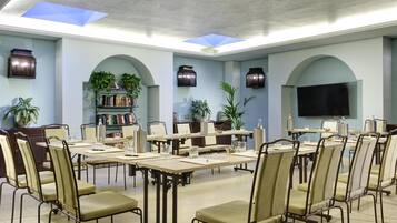 A conference room with tables and chairs, a bookshelf, potted plants, and a television.