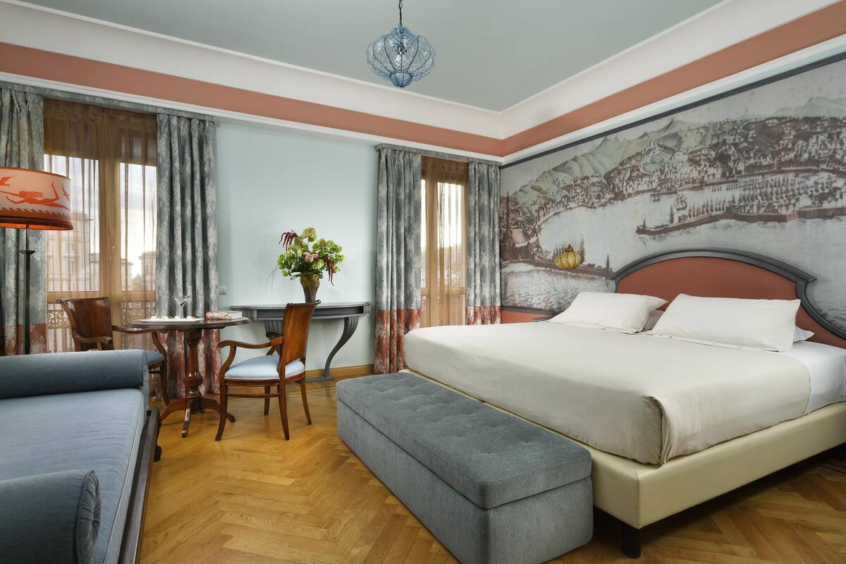 Habitación de hotel con cama, escritorio, silla, banco y un mural grande en la pared.