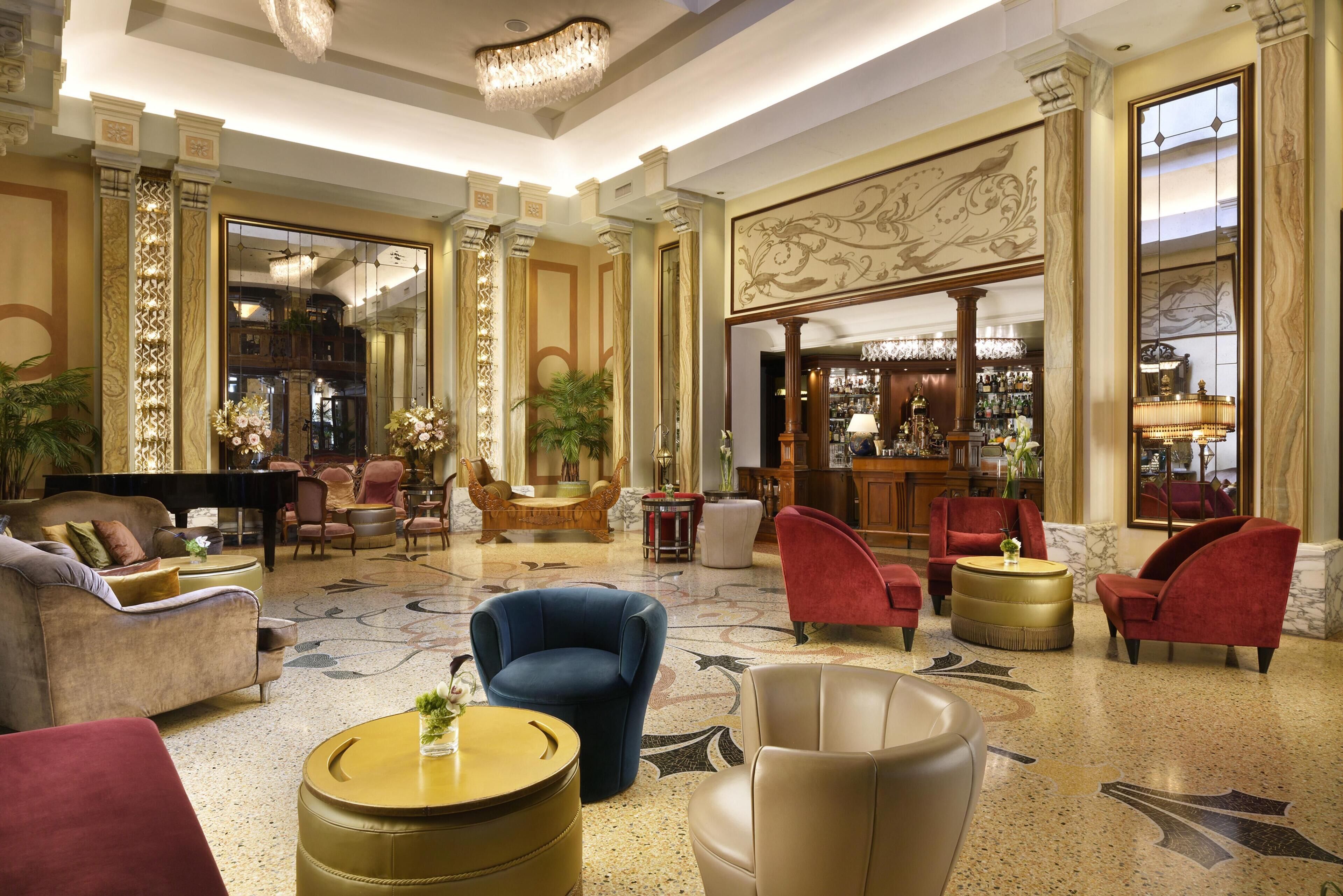 Een ruime lobby met een vleugelpiano, comfortabele zithoeken, een bar en decoratieve elementen.