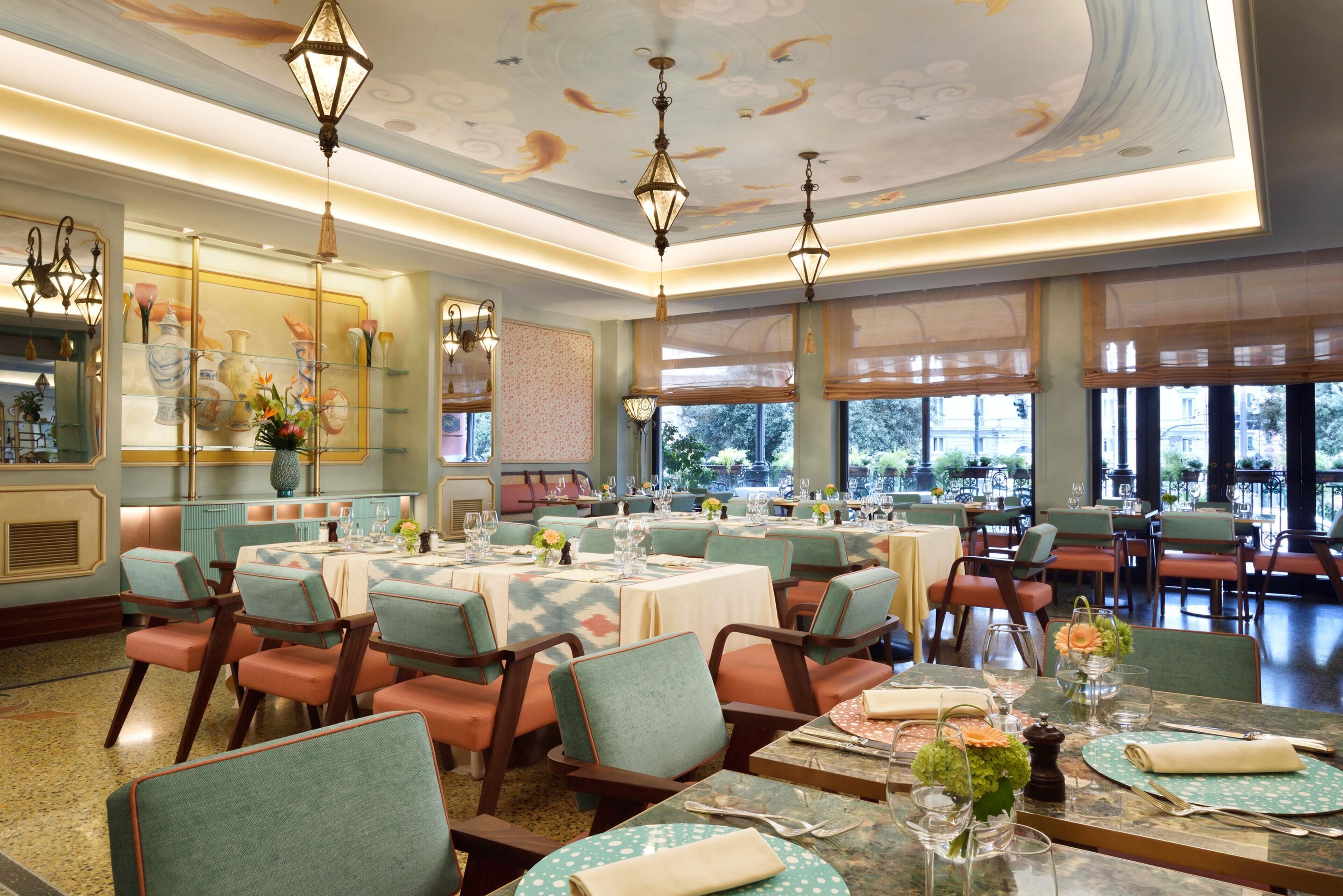 Un restaurant doté de nombreuses tables et chaises, d’un plafond décoratif et de grandes fenêtres.
