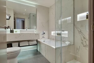 A modern bathroom with a marble sink, a large mirror, a glass-enclosed shower, and a toilet.