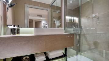 Un baño moderno con ducha envuelta en vidrio, un espejo grande y un tocador de madera con lavabo.