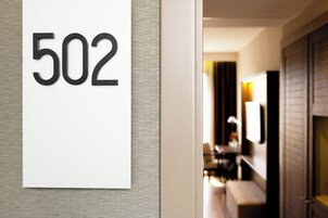 Quarto de hotel número 502 com design moderno, um espelho grande e uma área de estar visível ao fundo.
