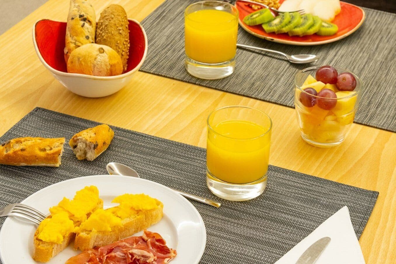 Une table mise pour le petit-déjeuner, avec du pain, des fruits et du jus.