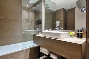 A modern bathroom with a glass-enclosed shower, a large mirror, a white sink, and a vanity with toiletries.