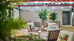A well-lit indoor seating area with multiple chairs and tables, surrounded by patterned walls and large potted plants. - Hesperia Sevilla (Seville)
