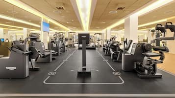 Un gimnasio moderno con diversas máquinas de ejercicio, una pantalla digital y un ambiente limpio e iluminado.