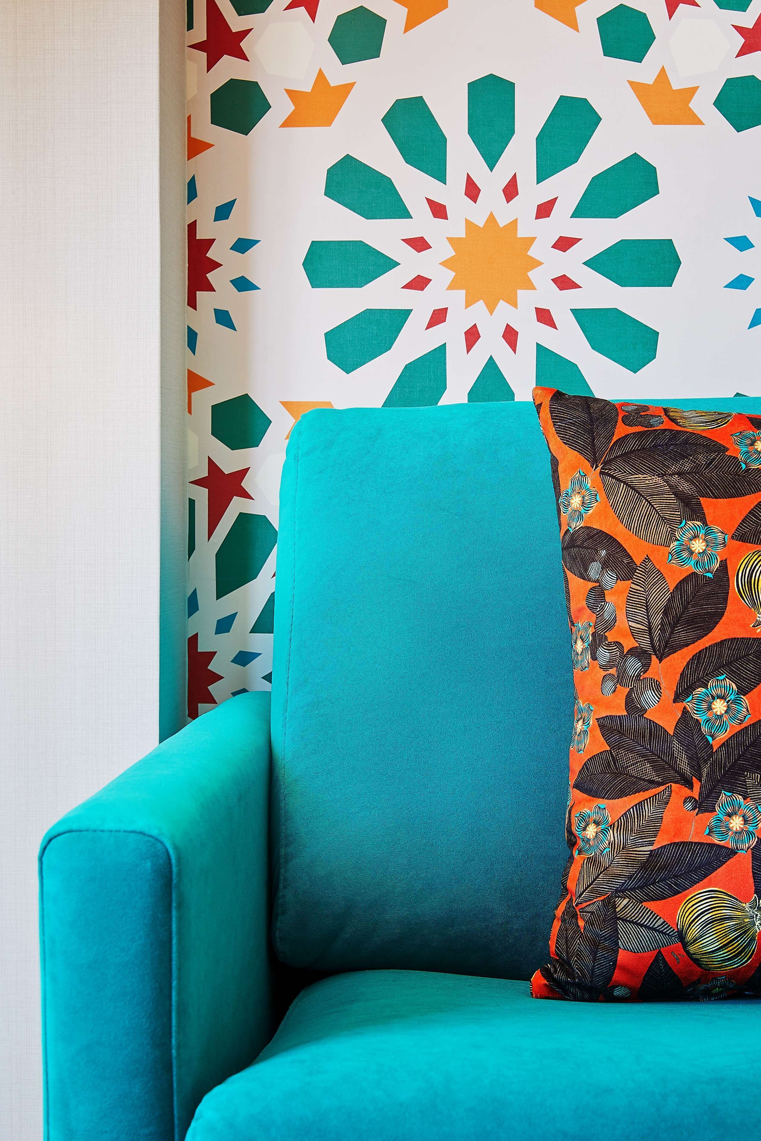 Una armchair color turquesa amb un coixí floral davant d'una paret amb un dibuix geomètric.