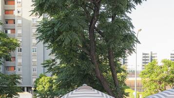 A swimming pool area with striped lounge chairs, a metal staircase, and a large tree in the background.