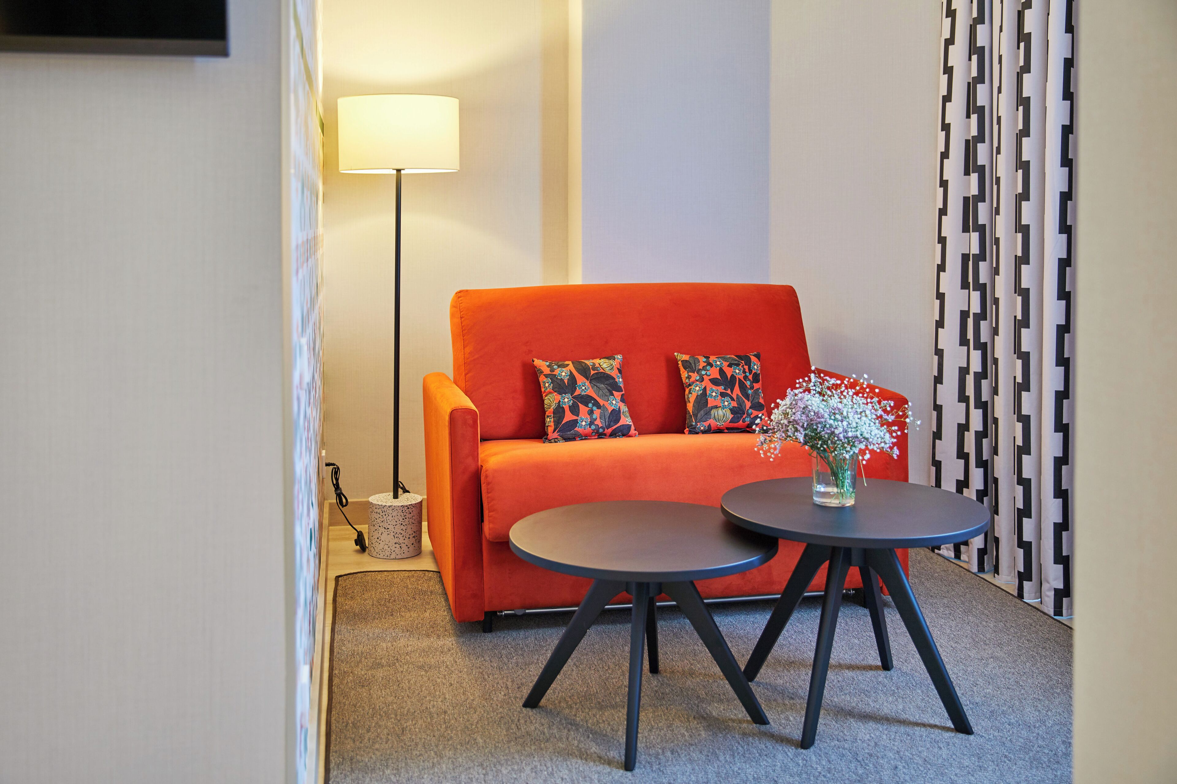 Een moderne woonkamer met een feloranje bank, twee zwarte tafels en een vloerlamp.
