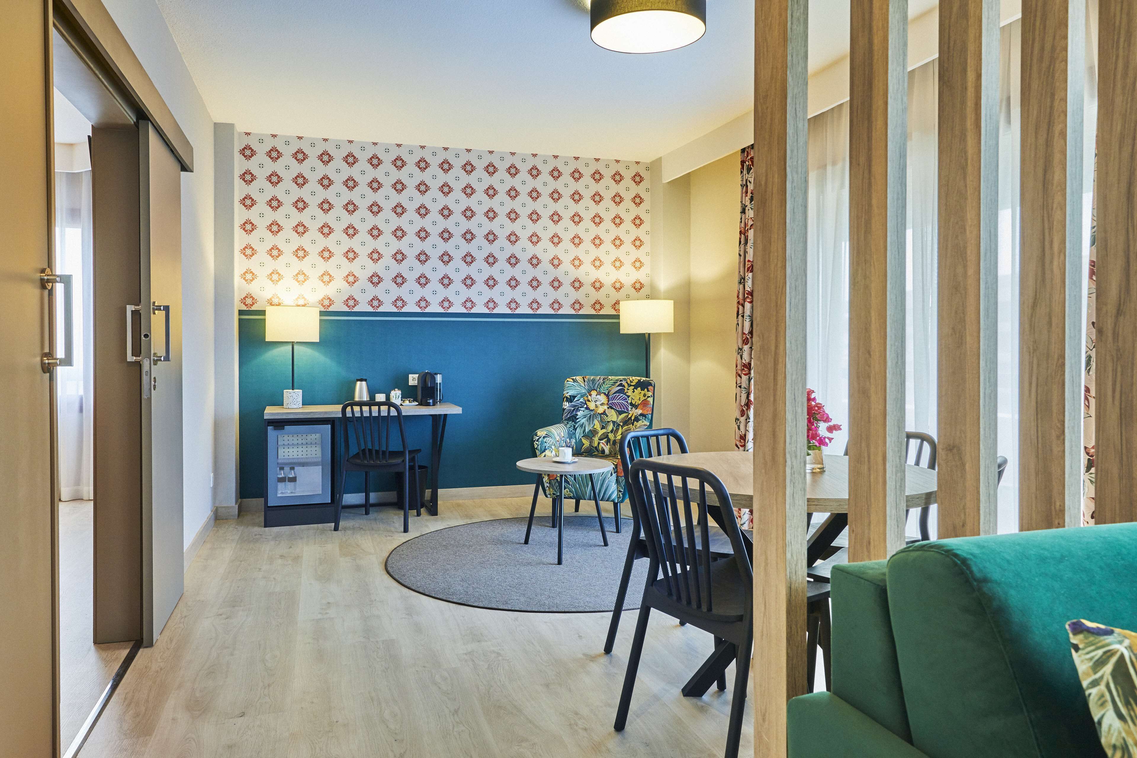 A modern living room with a green sofa, a dining area with a table and chairs, and a kitchen area with a fridge and a small island.