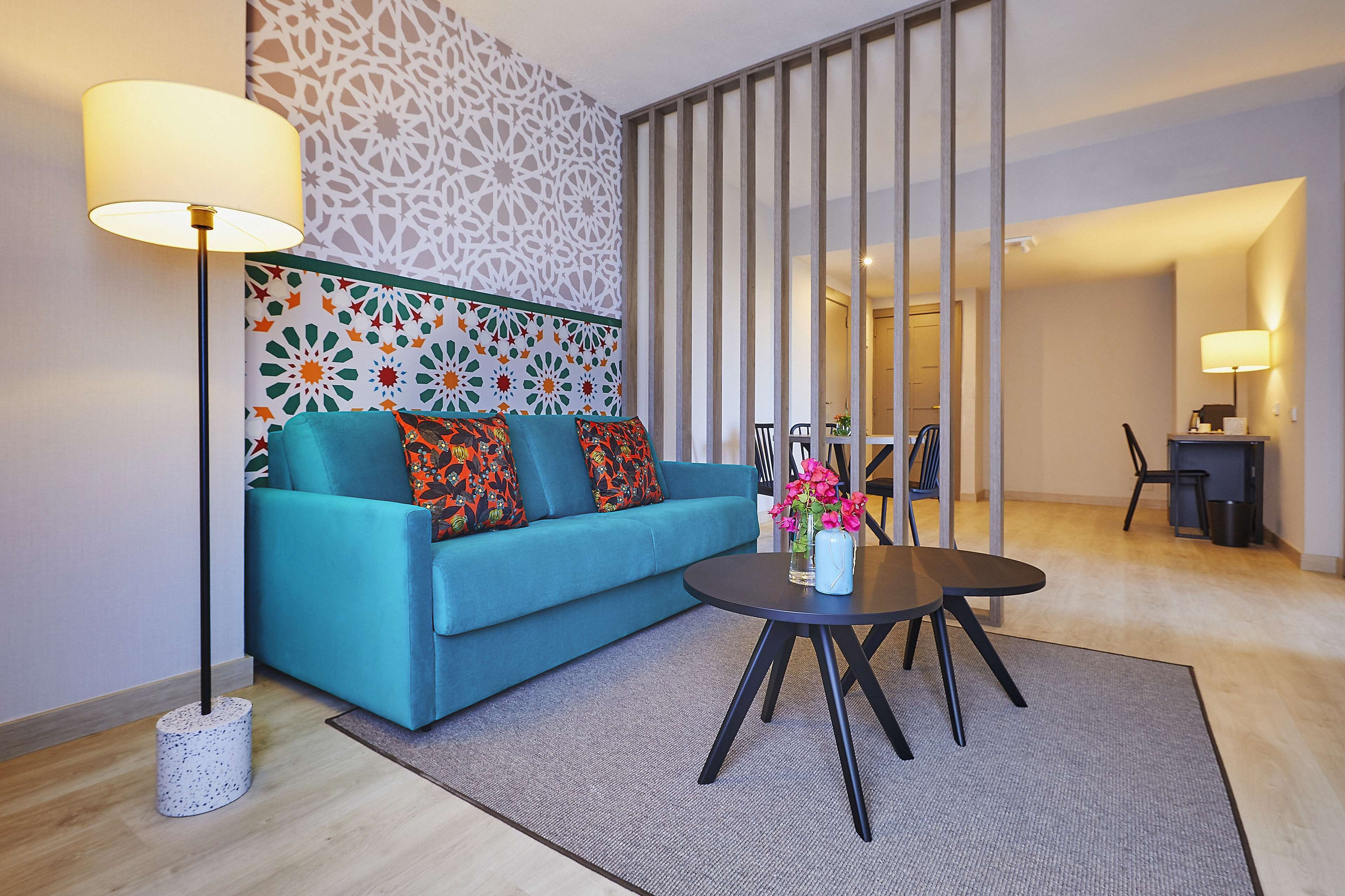 A modern living room with a teal sofa, a round coffee table, and a decorative wall.