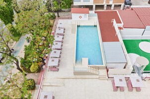 An aerial view of a hotel with a swimming pool, sun loungers, and a tennis court.