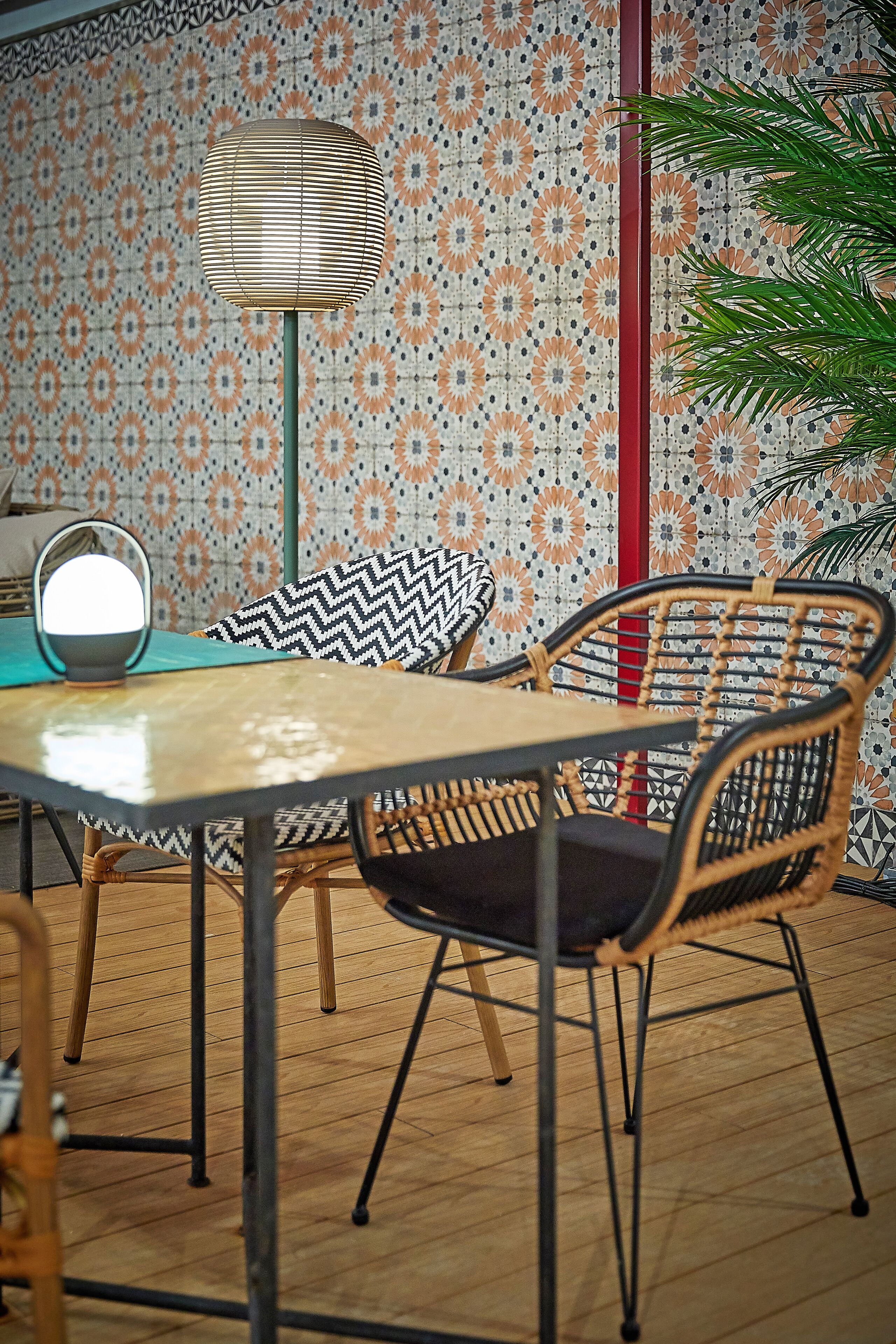 Un coin repas agrémenté d’un papier peint à motifs, d’une table avec des chaises, d’un lampadaire et d’une plante en pot.
