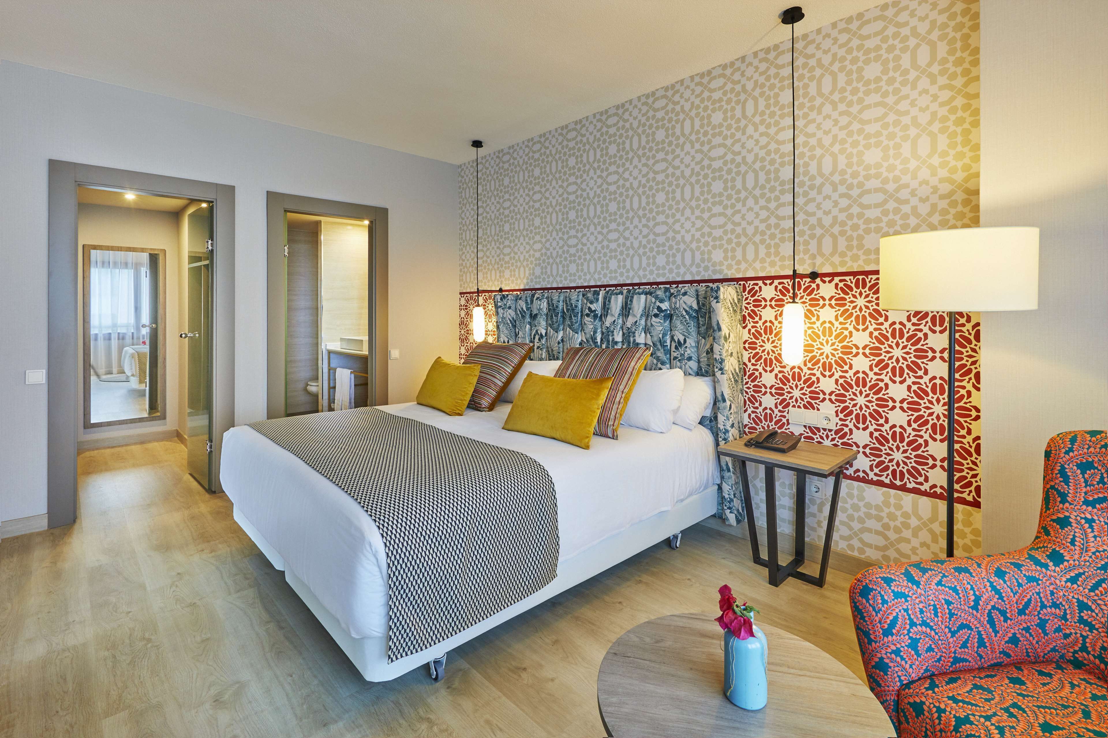 Een moderne hotelkamer met een groot bed, een klein tafeltje, een stoel en een decoratieve wand.