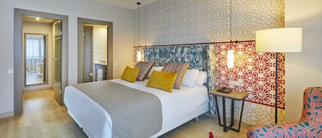 A modern hotel room with a large bed, a small table, a chair, and a decorative wall.