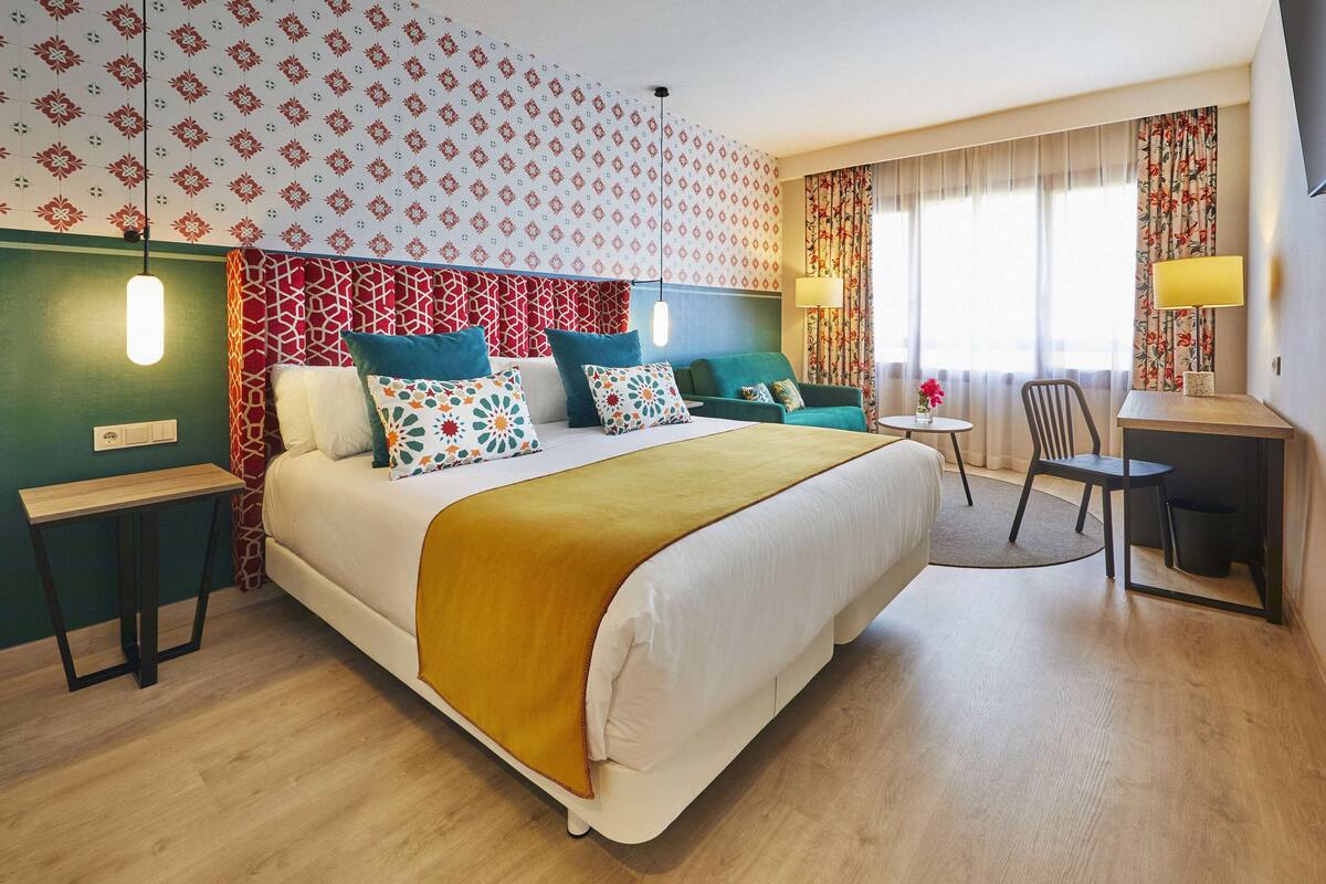 A hotel room with a large bed, a desk, a chair, and a small table.