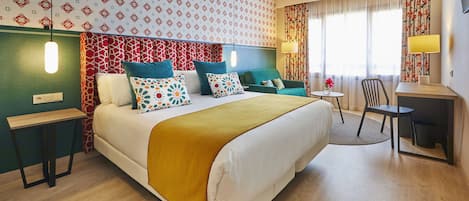 A hotel room with a large bed, a desk, a chair, and a small table.