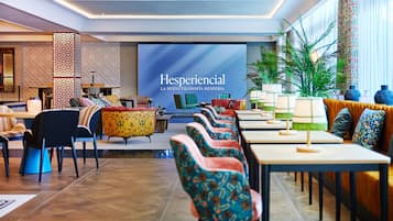 Un vestíbulo de hotel moderno con una pantalla grande que muestra 'Hesperiencial' y una zona de estar con sillas y mesas de colores.