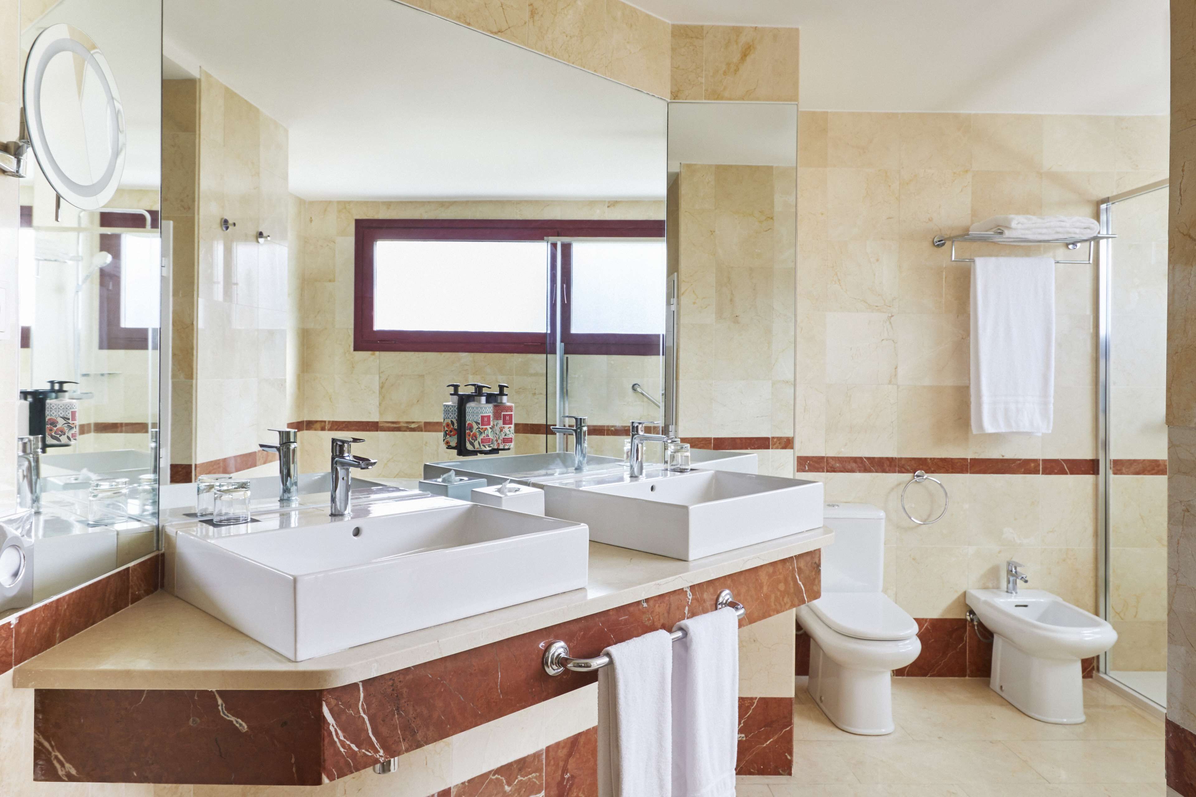 Un baño moderno con dos lavamanos, un inodoro, un bidé y un espejo grande.