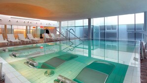 A modern indoor swimming pool with lounge chairs and a glass wall. - Hesperia Sevilla (Seville)