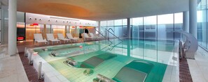 A modern indoor swimming pool with lounge chairs and a glass wall. - Hesperia Sevilla (Seville)