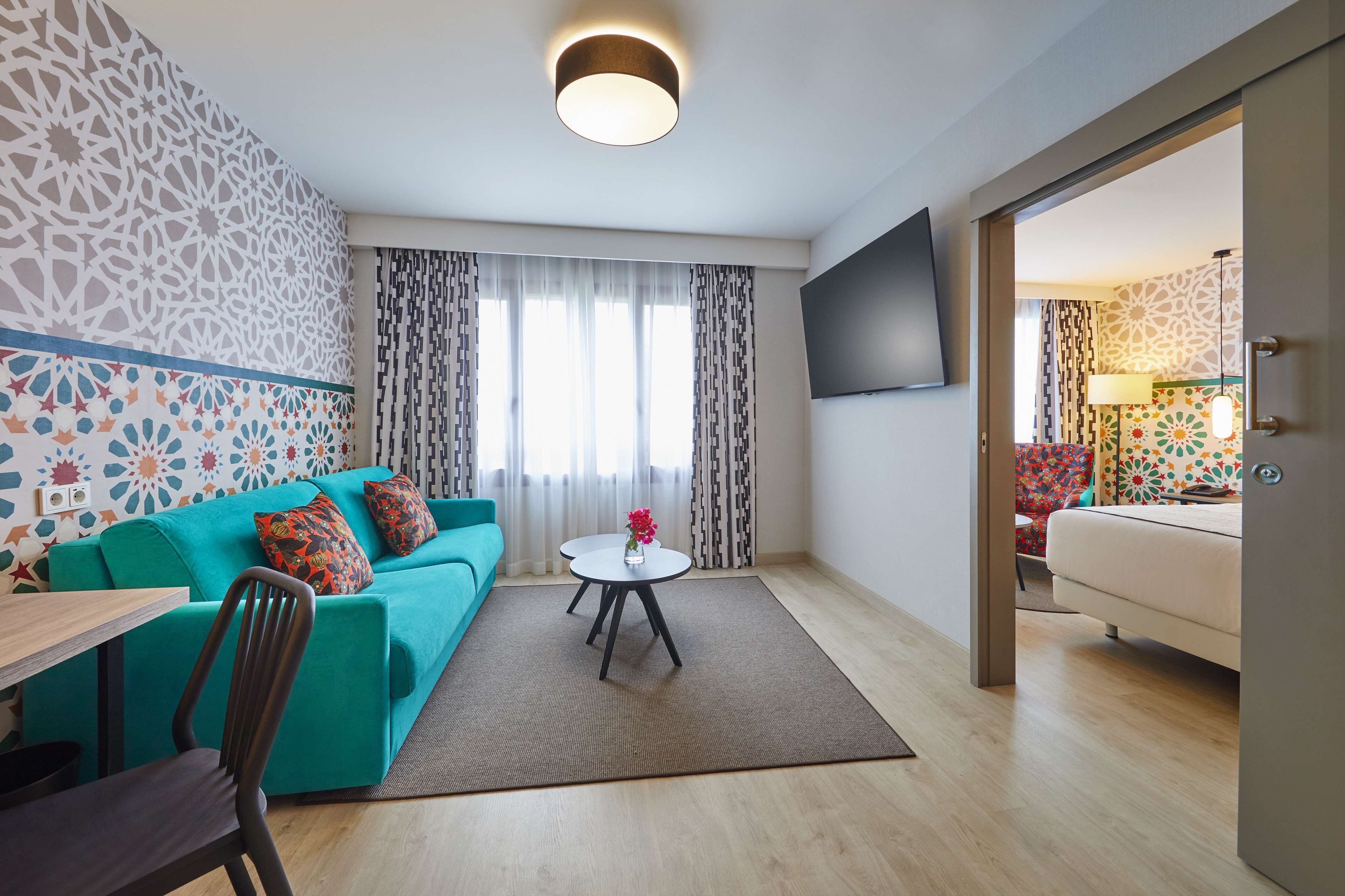 A modern living room with a teal sofa, a round coffee table, and a TV mounted on the wall.