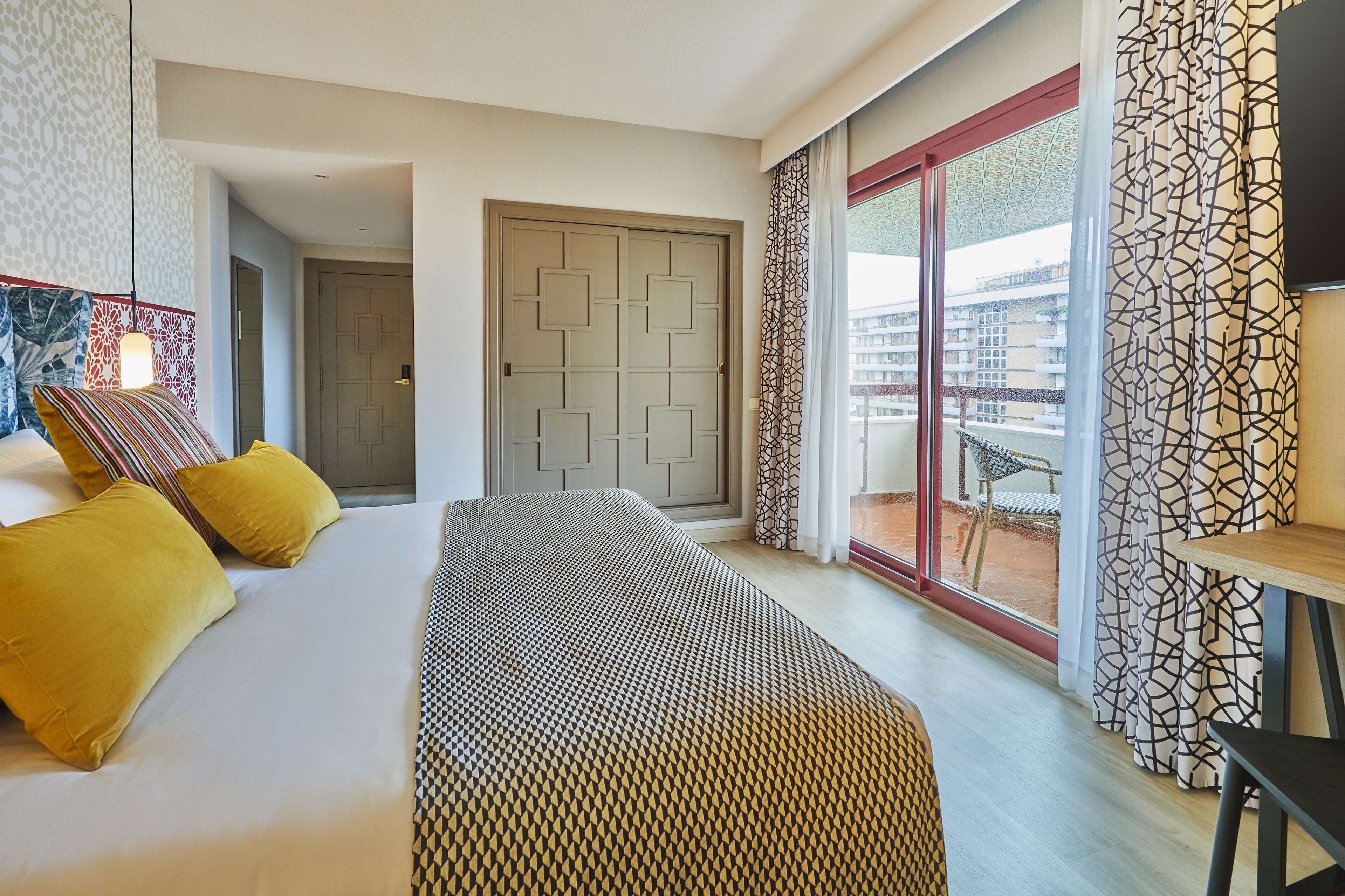Una habitación de hotel moderna con cama, un banco, una mesa de comedor y un balcón con vistas.