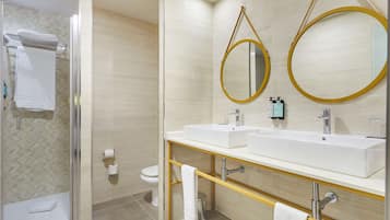 A modern bathroom with two sinks, a glass shower enclosure, and a toilet.